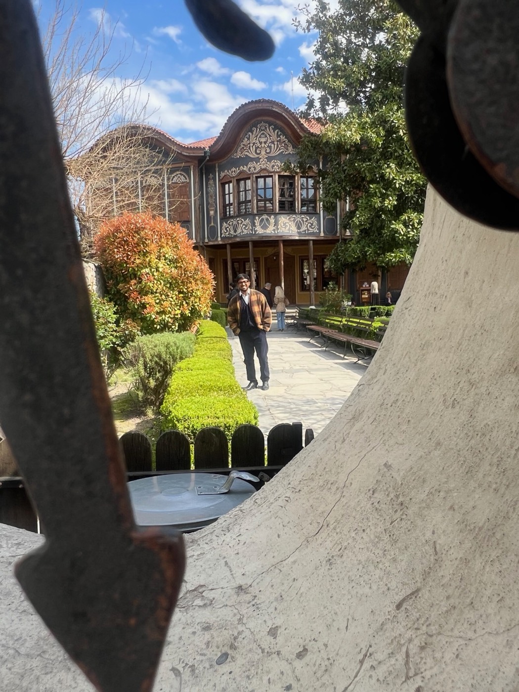 BhoumiK in a garden before a carved wooden house in Plovdiv