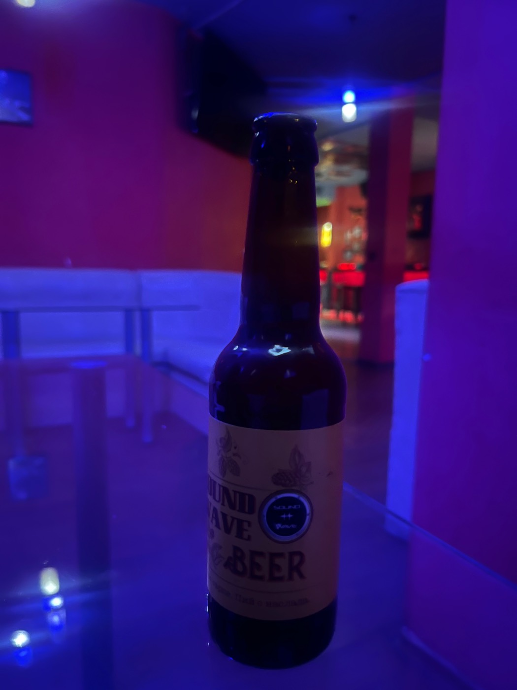 A bottle on a table under purple club lighting